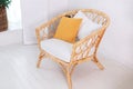 Design wicker wooden chair with pillows in stylish light bedroom interior. Rattan armchair by the white wall