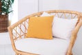 Design wicker wooden chair with pillows in stylish light bedroom interior. Rattan armchair by the white wall in the living room.
