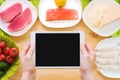 Design workpiece. Female hands hold a tablet PC over a table with raw seafood cheese and vegetables. Blank display for Royalty Free Stock Photo