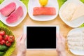 Design workpiece. Female hands hold a tablet PC over a table with raw seafood cheese and vegetables. Blank display for Royalty Free Stock Photo