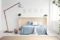 Designer lamp next to blue bed with blanket in white bedroom int Royalty Free Stock Photo