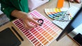 Designer with magnifying glass works with pantone scale in art studio.