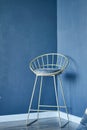 Designer modern chair on high legs, metal frame with soft cushion, seat. The chair is located in a corner with blue Royalty Free Stock Photo