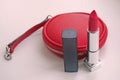 Designer red round leather purse with open lipstick on pink background