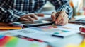 A designer sketching ideas on a tablet while seated at a workspace cluttered with creative materials during the afternoon Royalty Free Stock Photo