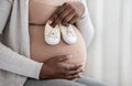 Desired Pregnancy. Black Pregnant Woman Embracing Belly And Holding Small Baby Shoes