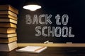 Desk against the background of the chalk board, books, notebook and pens, in the dark under the light of a lamp. Copy space