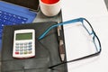 Desk with a calculator glasses, notepad and coffee.