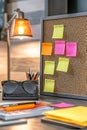 A desk with a cork board with yellow and orange sticky notes on it Royalty Free Stock Photo