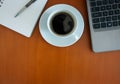 A desk with a cup of black coffee, laptop and a notepad with a pen Royalty Free Stock Photo