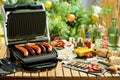 Desk with electric grill, grilled sausages and corn Royalty Free Stock Photo
