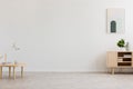 Desk lamp on a small table and a simple, wooden cabinet in an empty living room interior with white wall and place for a sofa. Rea Royalty Free Stock Photo