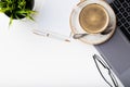 Desk with laptop, eye glasses, notepad, pen and a cup of coffee on a white table. Top view with copy space. Flat lay. Light backgr