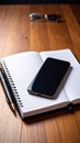 Desk setup with smartphone, notebook, pen, and glasses on a wooden surface for work or study. Royalty Free Stock Photo