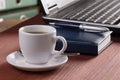 Desktop with coffee cup, opened laptop computer, diary, pan and document folders on background, no people, focused on coffee Royalty Free Stock Photo