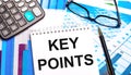 The desktop contains colored tables, a calculator, glasses, a pen and a notebook with the text KEY POINTS
