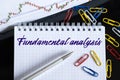 On the desktop are a forex chart, paper clips, a pen and a notebook in which it is written - Fundamental analysis