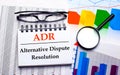 On the desktop are glasses, a magnifying glass, color charts and a white notebook with the text ADR Alternative Dispute Resolution Royalty Free Stock Photo