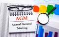 On the desktop are glasses, a magnifying glass, color charts and a white notebook with the text AGM Annual General Meeting.