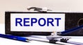 The desktop has a stethoscope, a blue pen, and a gray file folder with the text REPORT. Medical concept Royalty Free Stock Photo