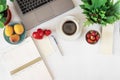 Desktop with laptop, weekly notebook, pen, coffee, fruit, flowers, top view