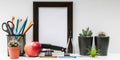 Empty dark photo frame, succulents in dark pots, colored pencils, office supplies, red apple on a white background. Desktop MockUp