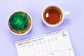 Desktop paper calendar for December 2022 and a flower in a pot on a light lilac background.
