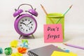 On the desktop there is a bio-alarm clock, a pencil holder, a notebook. The pink sticker says - don't forget Royalty Free Stock Photo