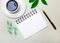 On the desktop is a white cup with coffee, a green plant and paper clips, a pen and a blank notebook with a place to insert text. Royalty Free Stock Photo