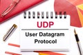 On the desktop is a white notebook with the text UDP User Datagram Protocol, a pen, burgundy and red tables, and gold-framed