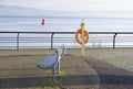 Desolate beach esplanade with empty seat bench and orange water safety buoy ring