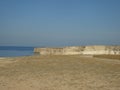 A desolate plain with a steep rocky coast and a huge cloudless blue sky.