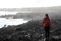 Desolate volcanic black rocks with lonely girl. Back view of young woman standing reflexive and sad on hidden rocky beach. Young