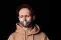 Close-up portrait of young emotive man with three colors duct tape over his mouth isolated on dark background Royalty Free Stock Photo