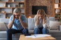 Despaired sad middle aged european couple suffer from bills in living room interior