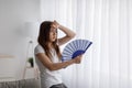 Despaired tired millennial caucasian lady suffering from heat waves blowing fan at herself, wipes sweat with hand Royalty Free Stock Photo