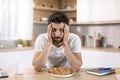 Despaired tired millennial caucasian man with beard holds head with hand, asleep at table with croissant