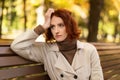 Despaired unhappy young european red-haired lady in raincoat suffers from headache, loneliness sits on bench Royalty Free Stock Photo