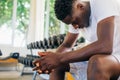 Desperate African American man sitting on bench during break in fitness training in modern gym