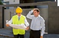 Desperate customer in stress and constructor foreman worker with helmet and vest arguing outdoors on new house building blueprints