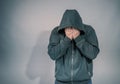 Desperate man in hooded jacket is crying, hands are covering face and tears in the eyes, light of hope shining from his right side