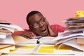 Desperate nervous dark skinned male student looks stressfully at pile of papers, writes information in notepad, has Royalty Free Stock Photo