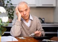 Gray haired old man sitting at table and counting coins and money