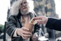 Grey-haired homeless man carrying cardboard cup and begging