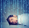 Desperate stressed man resting head on laptop with binary code falling down