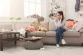 Desperate woman sitting on sofa in messy room