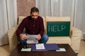 Desperate young man calculating household expenses sitting on the couch and asking for help on a blackboard