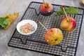 Dessert, caramelized candy apples in transparent caramel, sprinkled with sugar decor, on a black grate on a gray concrete Royalty Free Stock Photo