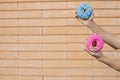 Close-up of a pink doughnut with red cherry and sprinkle glaze and a blue donut with beads held by an american male hand