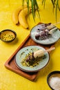 Dessert, frozen chocolate covered bananas with coconut or sugar sprinkles on a green ceramic plate on a yellow concrete background